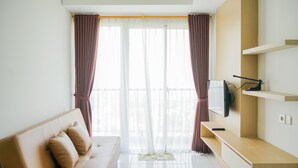 Ein modernes Wohnzimmer mit einer Couch, einem Flachbildfernseher, der an einem Holzregal befestigt ist, und einem großen Fenster mit transparenten Vorhängen.