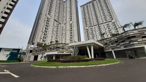 A modern high-rise residential building with a central courtyard and a landscaped area with plants. - Studio @ Akasa Pure Living Apartment BSD (South Tangerang)