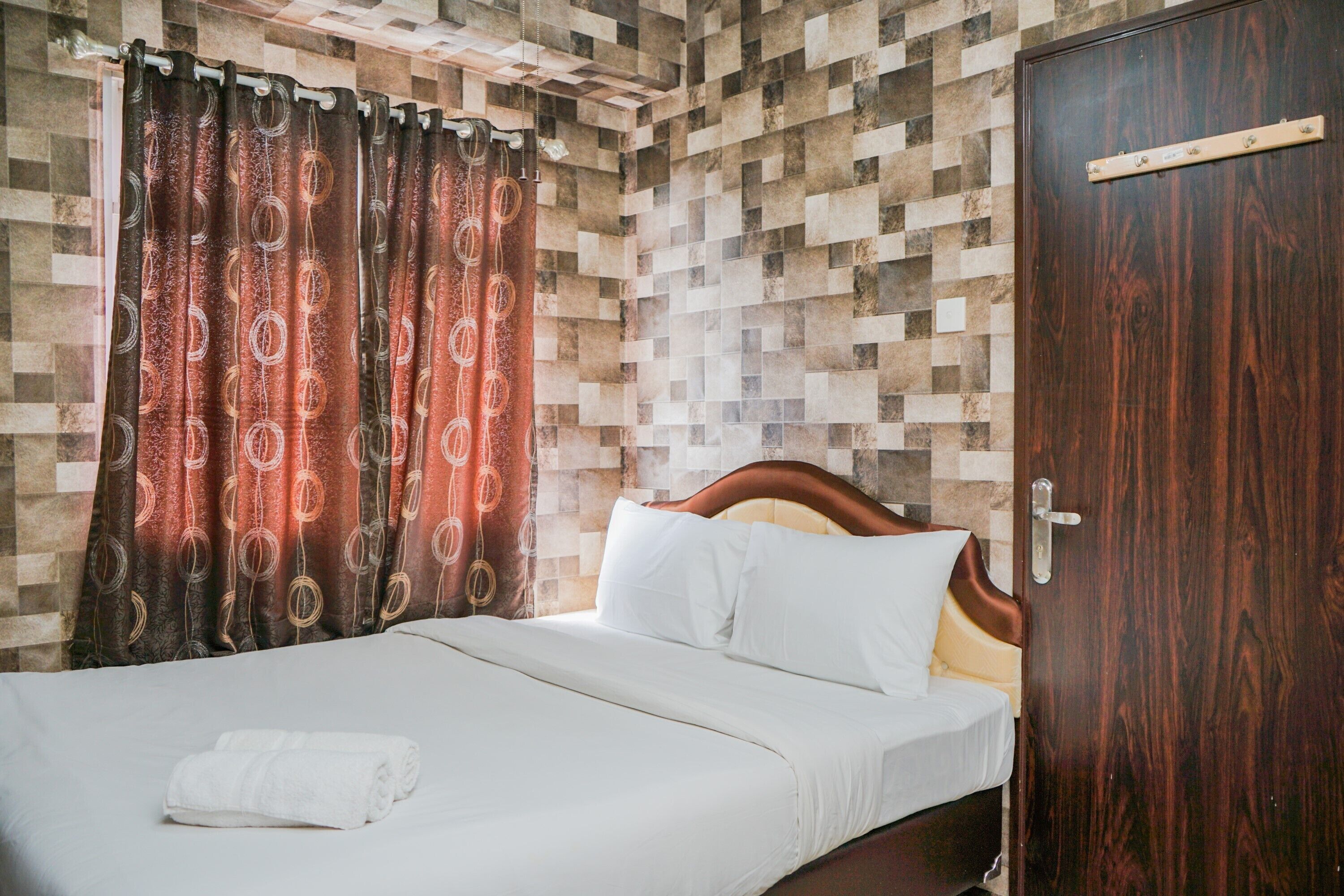 A neatly made bed with white linens and a rolled towel, a wooden headboard, and a door with a handle.