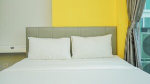A bed with white bedding and pillows, a grey headboard, and a yellow wall. - Highest Value 1BR Apartment at Tree Park BSD (South Tangerang)