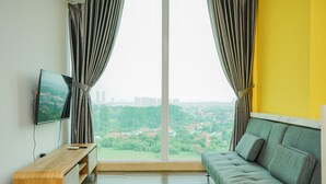 A room with a large window, a TV on a wooden stand, a green sofa, and a yellow wall. - Highest Value 1BR Apartment at Tree Park BSD (South Tangerang)