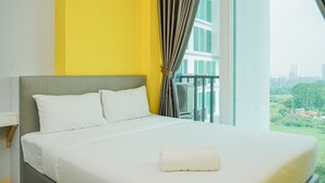 A hotel room with a large bed, white bedding, a grey headboard, and a view of a cityscape through a window with curtains. - Highest Value 1BR Apartment at Tree Park BSD (South Tangerang)