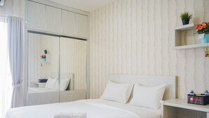 Une chambre d’hôtel bien rangée, avec un grand lit, une table de chevet, un miroir et une étagère sur laquelle se trouvent une plante et une boîte de produits de toilette.