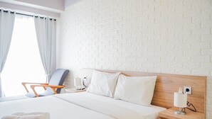 Une chambre d’hôtel avec un grand lit, une tête de lit en bois, une table de chevet avec une lampe, une chaise et une fenêtre avec des rideaux.