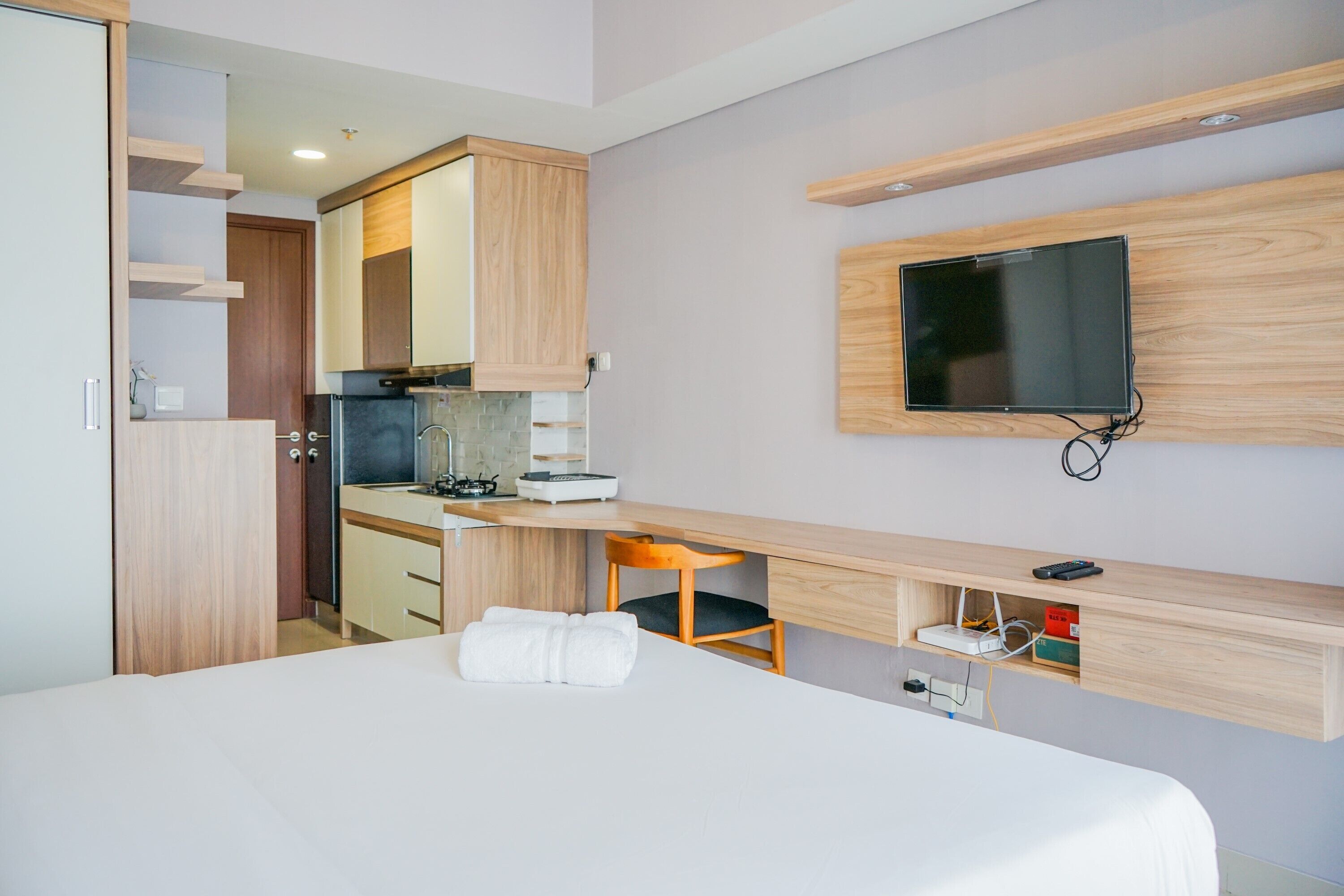 Una habitación de hotel moderna con cama, kitchenette, televisor montado en la pared y un escritorio de madera.