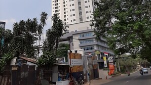 Un grand immeuble moderne à plusieurs étages, entouré de verdure et donnant sur une rue où circulent des véhicules.