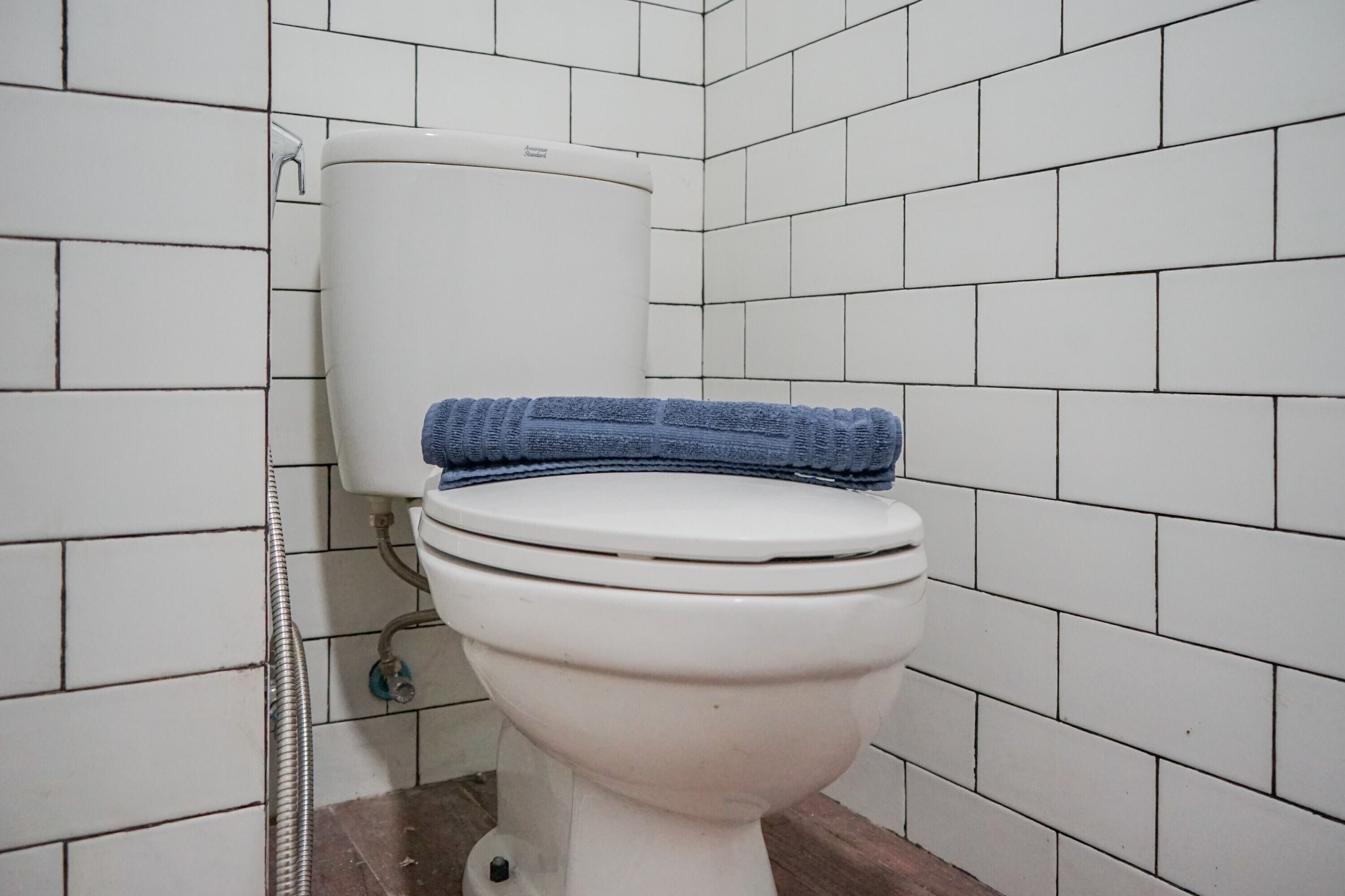 A toilet with a blue towel on top, set against a white tiled wall.