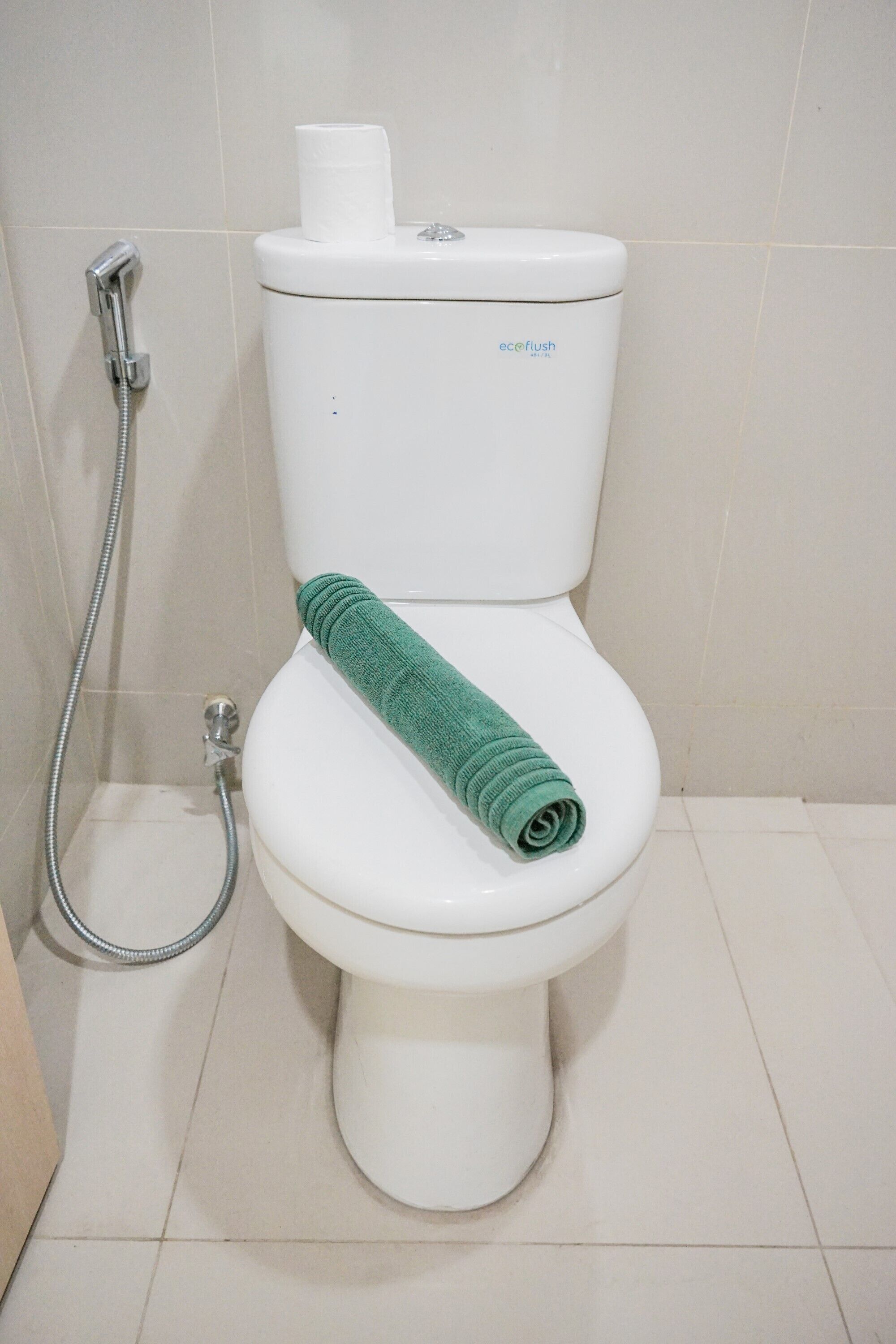 WC, jossa on vihreä pyyhe, WC-paperiteline ja suihkuletku.