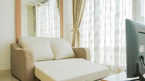 A modern living room with a sofa, a flat-screen TV, and a window with sheer curtains. - Wonderful Studio Apartment at Tree Park (South Tangerang)