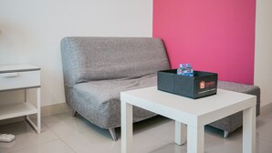 A room with a grey sofa, a white table, and a traveler's box on the table. - Cozy and Relax Studio Room @ Tree Park BSD Apartment (South Tangerang)