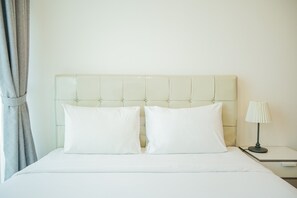 A neatly made bed with two pillows and a bedside table with a lamp. - Cozy and Relax Studio Room @ Tree Park BSD Apartment (South Tangerang)