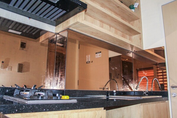 A kitchen with a black countertop, stainless steel appliances, and wooden cabinets. - Minimalist and Cozy Studio Room at Ayodhya Apartment (Tangerang)