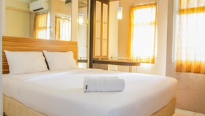 A neatly made bed with white linens and a folded towel, a wooden headboard, and a large mirror above the bed. - Compact and Mini Studio Great Western Resort Apartment (Tangerang)