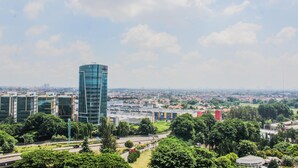 A modern urban landscape with a prominent glass skyscraper, surrounded by greenery and other buildings. - Compact and Mini Studio Great Western Resort Apartment (Tangerang)