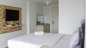 A hotel room with a bed, a television mounted on the wall, a small kitchenette, and a bathroom visible through an open door. - Minimalist Studio Apartment at Poris 88 with City View (Tangerang)