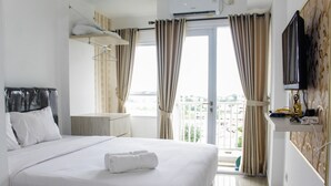 A hotel room with a bed, a desk, a television, and a balcony with curtains. - Minimalist Studio Apartment at Poris 88 with City View (Tangerang)