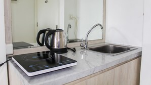 A kitchen with a built-in induction cooktop, a kettle, and a sink. - Minimalist Studio Apartment at Poris 88 with City View (Tangerang)