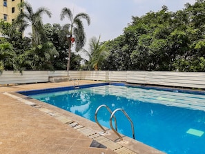 Une piscine à l’eau d’un bleu cristallin, entourée d’une terrasse carrelée et d’une rambarde en métal.