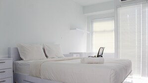 Ein modernes Schlafzimmer mit einem Bett, einem Nachttisch, einer Kommode und einem Fenster mit Jalousien.