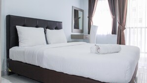Cama bem arrumada com lençóis brancos, cabeceira escura e toalha enrolada no pé da cama.