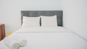 A neatly made bed with white linens and pillows, a wooden nightstand with a yellow object, and a grey headboard. - New Furnished 2BR near CGK Airport @ Ayodhya Apartment (Tangerang)