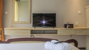 Una camera d'albergo con un letto, una televisione su un supporto in legno, uno specchio e un piccolo box con un telecomando sul supporto.