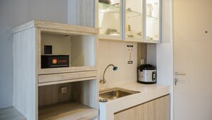 A compact kitchen with a sink, a stove, and a cabinet with glass doors. - Comfortable Studio Apartment at Ayodhya Residences (Tangerang)