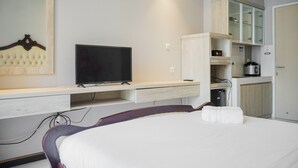 Ein Hotelzimmer mit Bett, Fernseher, einer kleinen Küchenzeile und einem Spiegel.