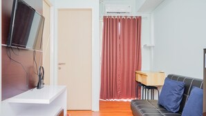 Ein modernes Wohnzimmer mit einem an der weißen Wand montierten Flachbildfernseher, einem schwarzen Sofa mit blauen Kissen, einem Holztisch und einem roten Vorhang.