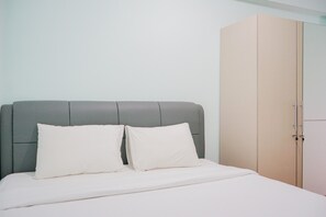 Ein Bett mit grauem Kopfteil und weißer Bettwäsche, ein beiger Kleiderschrank und ein weißes Schränkchen.