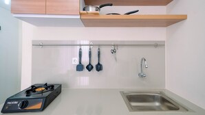 A kitchen with a gas stove, a sink, wooden shelves above the counter, and various kitchen utensils hanging on a rack.
