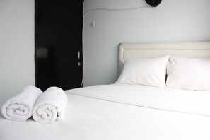 A neatly made bed with white linens and pillows, a black door, and a wall-mounted light fixture. - Quite 2BR Apartment at The Jarrdin Cihampelas (Bandung)
