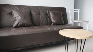 A modern living room with a dark brown leather sofa, two matching cushions, and a small wooden side table. - Quite 2BR Apartment at The Jarrdin Cihampelas (Bandung)