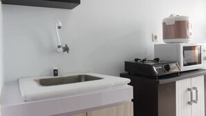 A kitchen with a sink, a microwave, and a rice cooker on the countertop. - Quite 2BR Apartment at The Jarrdin Cihampelas (Bandung)