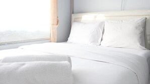 A neatly made bed with white linens in a room with a large window and a view of the cityscape. - Modest 2BR Apartment at The Jarrdin Cihampelas (Bandung)
