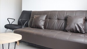 A brown leather sofa with two cushions, a small round table, and a black chair. - Modest 2BR Apartment at The Jarrdin Cihampelas (Bandung)