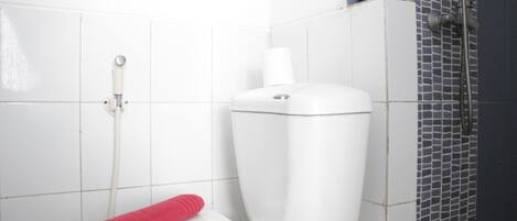 Et hvidt toilet med et rødt håndklæde, toiletpapirholder og brusehoved på væggen.