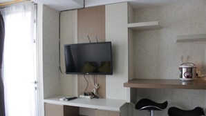 A modern room with a flat-screen TV mounted on the wall, a coffee maker on a shelf, and two bar stools. - Homey 2BR Apartment at The Jarrdin Cihampelas (Bandung)