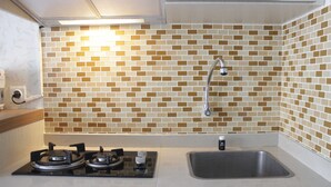 A kitchen with a gas stove, a sink, and a backsplash made of small, square tiles in various shades of brown and beige. - Homey 2BR Apartment at The Jarrdin Cihampelas (Bandung)