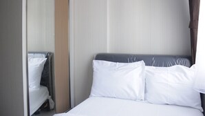 A hotel room with a bed, white linens, a mirror, and a striped wall. - Homey 2BR Apartment at The Jarrdin Cihampelas (Bandung)