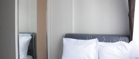 A hotel room with a bed, white linens, a mirror, and a striped wall.