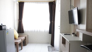 A compact room with a kitchenette, a small dining area with two chairs, a television mounted on the wall, and a window with curtains. - Homey 2BR Apartment at The Jarrdin Cihampelas (Bandung)