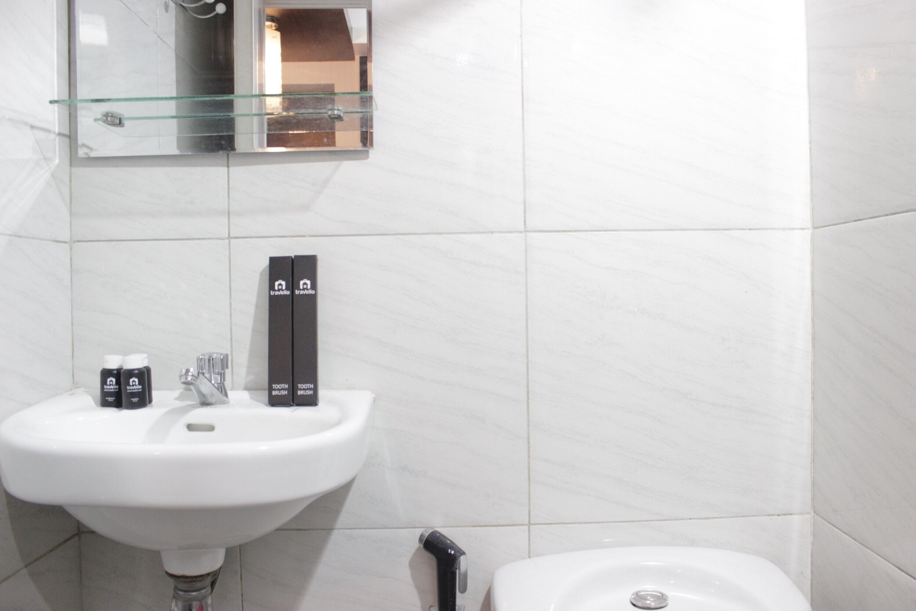 Een badkamer met een witte wastafel, een glazen plank erboven en een toilet.