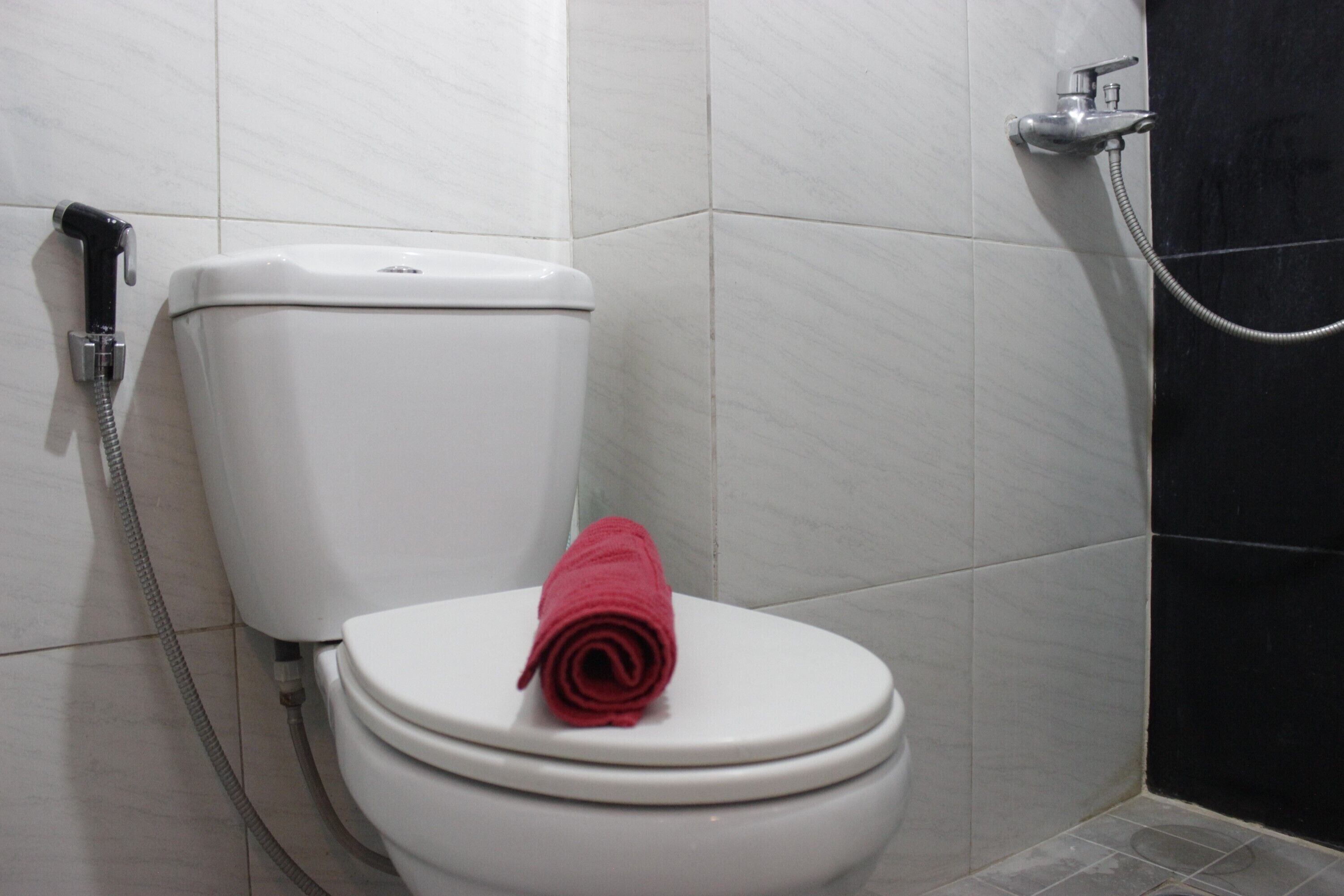 Des toilettes blanches avec une serviette rouge posée sur la lunette, une douchette et un porte-rouleau de papier toilette.