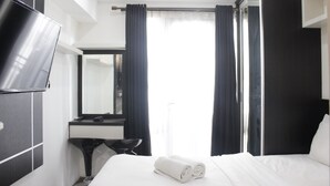 Habitación de hotel con cama, televisor, escritorio y espejo.
