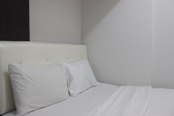 A bed with white bedding and pillows, a headboard with buttons, and a plain wall.