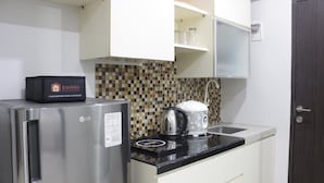A compact kitchen with a stainless steel refrigerator, a kettle, and a coffee maker on the countertop.