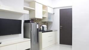 A modern kitchen with white cabinetry, a stainless steel refrigerator, a flat-screen TV, and a dark wooden door.