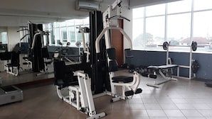 Un gimnasio con diverso equipo de ejercicio, ventanas amplias y un espejo.