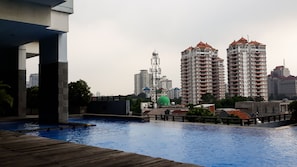 A swimming pool with a wooden deck, surrounded by high-rise buildings and a green dome structure. - Cozy and Minimalist 2BR at Marbella Kemang Apartment (Jakarta)